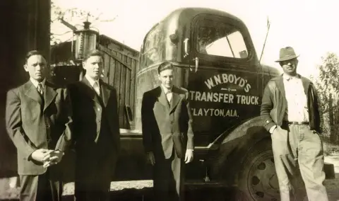 Cecil Boyd, at left, and his brothers Hilly and Dempsey, stand next to a tractor their father, William Nickey Boyd, right, operated. Following World War II, the Boyd brothers drove trucks for 10 years before starting their own company – Boyd Brothers in 1956. (Photo: Business Wire)